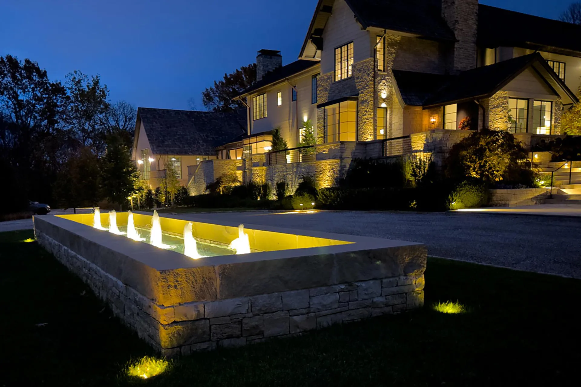 A luxury home at dusk with an illuminated fountain and outdoor lighting.