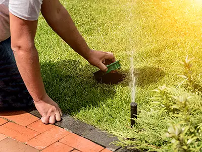 An Aqueduct Irrigation technician adjusting a sprinkler head in a green lawn during a spring irrigation startup in Nashville, Tennessee