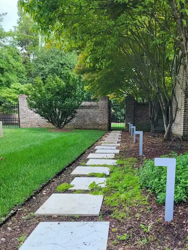 Modern low-voltage path lights lining a stone paver walkway beside a brick garden wall